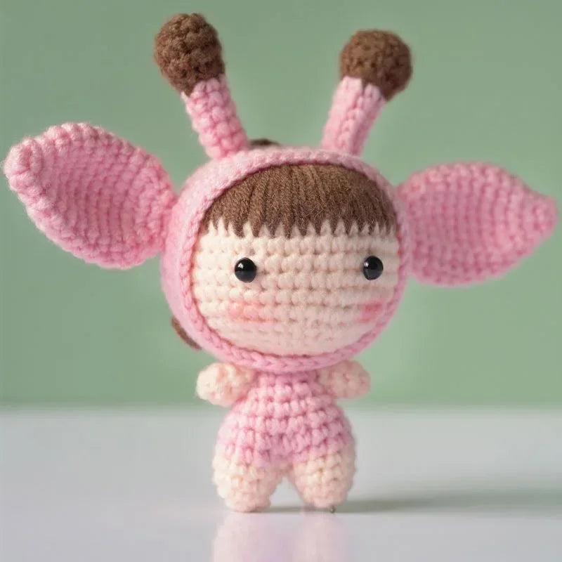 A handmade crochet doll kit featuring pink ears and a brown face, displayed against a light green background.