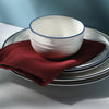 A white ceramic bowl and matching plate set with a deep red napkin resting on them.
