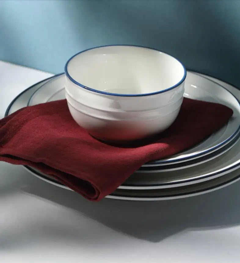 A white ceramic bowl and matching plate set with a deep red napkin resting on them.