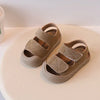 A pair of tan suede toddler soft-soled sandals for boys and girls resting on a light colored surface.