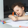 A young boy is holding an orange retractable water spray pen and writing on paper.