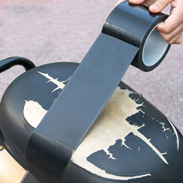 A hand is applying a strip of dark gray self-adhesive leather repair tape to the lid of a black pot.