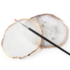 A round, translucent white resin palette with a gold trim and a thin brush resting on it.