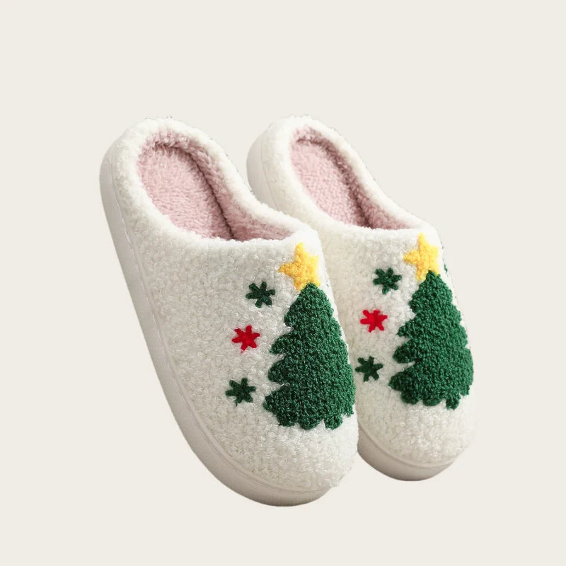 A pair of white plush indoor slippers decorated with green Christmas trees and yellow stars.
