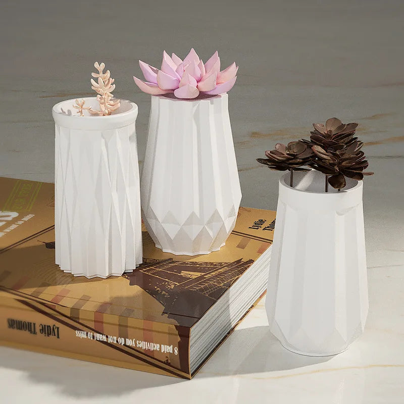 White ceramic flower pots with pink and brown floral designs displayed on a book.