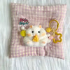 A white silicone hamster squishy toy with yellow accessories is sealed in a clear plastic bag against a pink checkered fabric