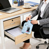 A woman is using a portable hot water bottle with a cozy cover on a wooden desk.