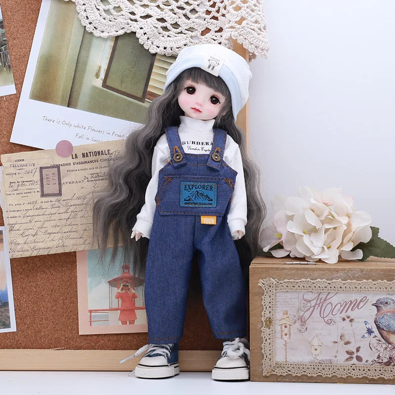 A doll dressed in a denim outfit and a white bonnet stands next to a box of flowers.