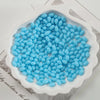 A pile of light blue oval glass rice grain beads for jewelry making in a white dish.