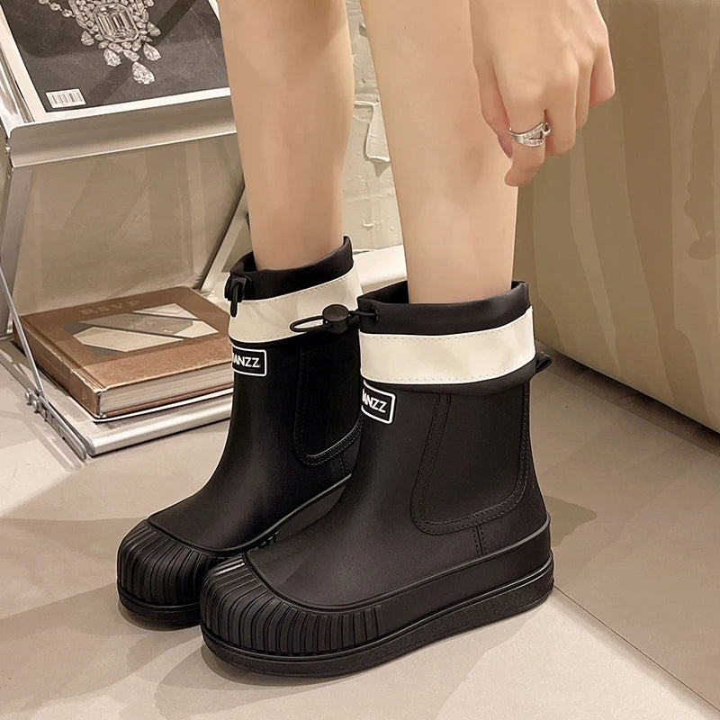 A pair of black waterproof mid-calf rain boots with white trim and non-slip soles are shown on a light surface.