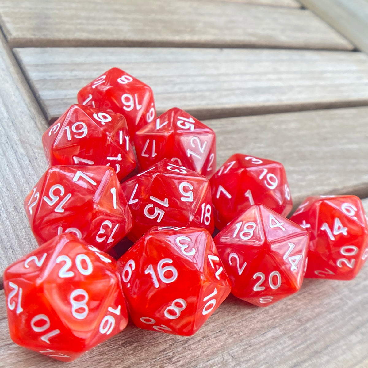 A collection of ten red acrylic D20 dice scattered on a wooden surface.