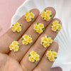 A hand holds several small resin flower ornaments in yellow and green colors.