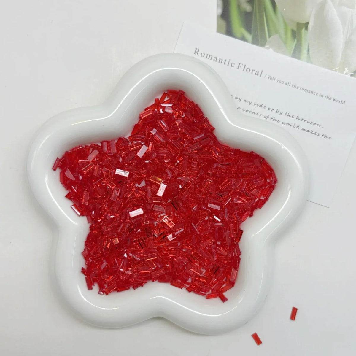 A white heart-shaped container filled with red glitter acrylic filler for nail art and DIY crafts