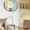 A round analog teaching clock with colorful numbers and hands mounted on a light beige wall.
