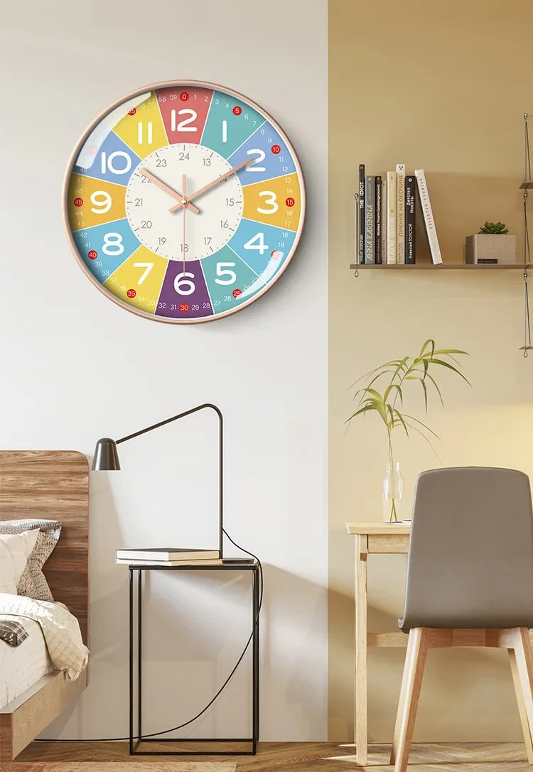 A round analog teaching clock with colorful numbers and hands mounted on a light beige wall.