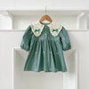 A teal cotton party dress for girls featuring lace collar details and embroidered bows, displayed on a white shelf.