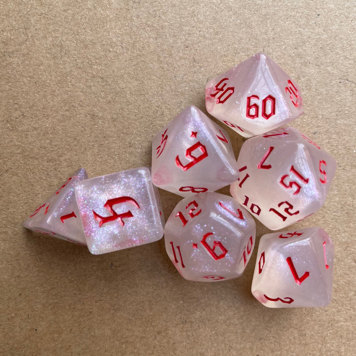 A set of seven pink glitter polyhedral dice, including a d10 and d6, resting on a brown surface.