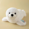 A white, fluffy seal plush toy with black eyes and a small tag is shown against a light background.