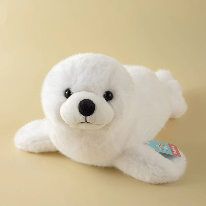 A white, fluffy seal plush toy with black eyes and a small tag is shown against a light background.