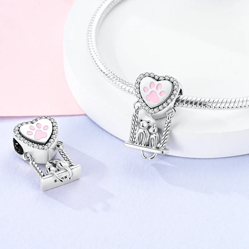 A silver heart charm bead with a pink zirconia detail is displayed on a white jewelry display.
