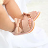 A close-up of a baby's foot wearing light pink summer sandals with soft anti-slip soles and bowknot details.