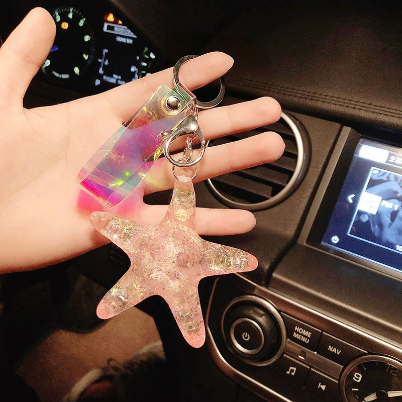 A hand holds a clear, pink starfish beaded keychain attached to a metal ring.