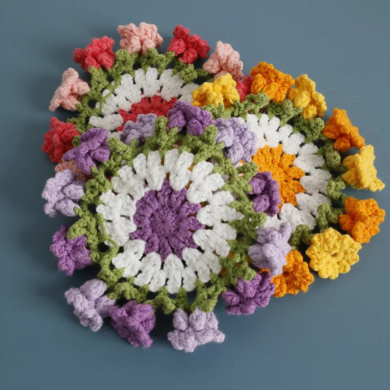 A circular arrangement of hand-crocheted floral coasters in various shades of pink, purple, yellow, and green.