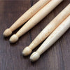 A set of light-colored maple drumsticks laid diagonally on a dark wooden surface.