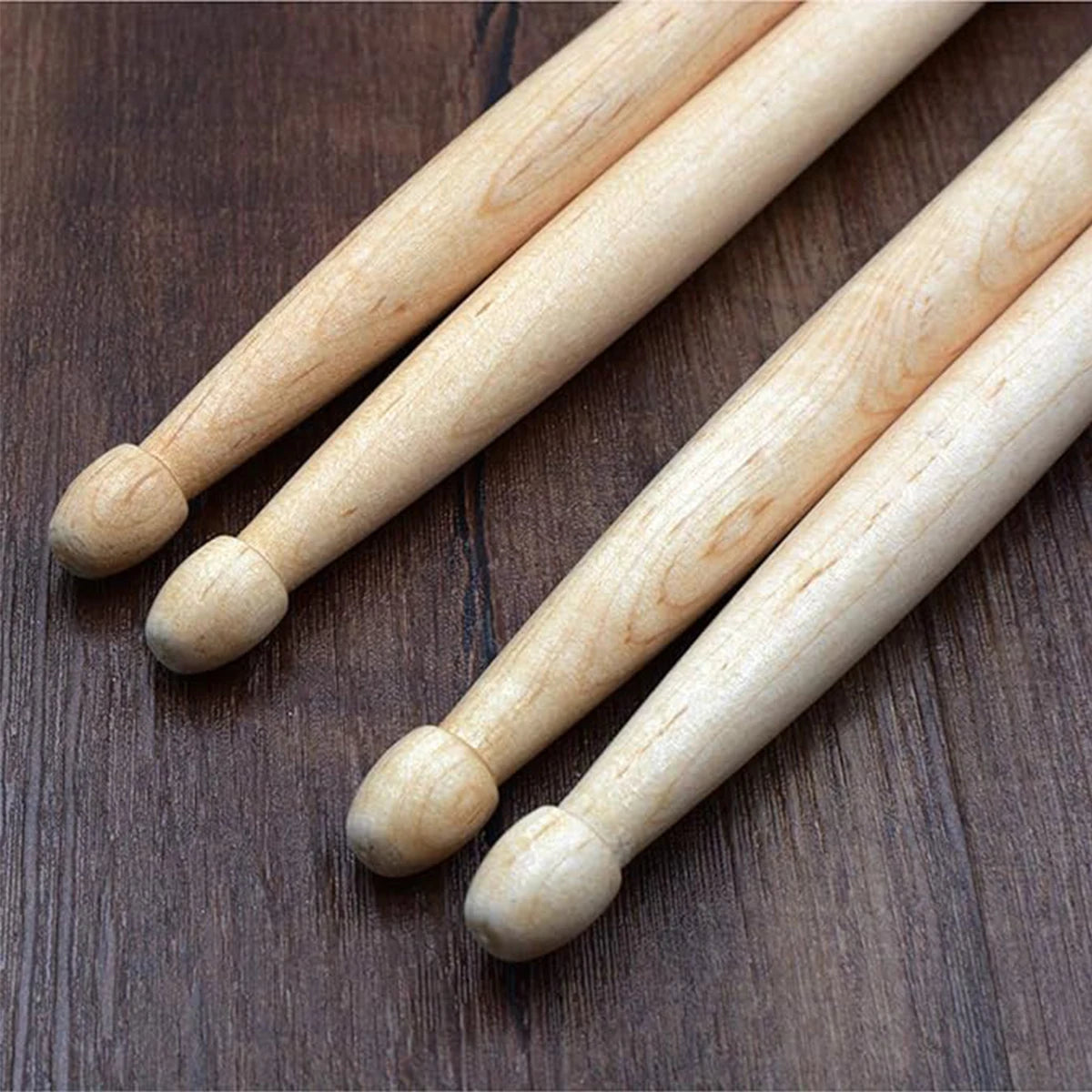 A set of light-colored maple drumsticks laid diagonally on a dark wooden surface.