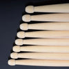 A set of light-colored maple wood drumsticks arranged in a vertical line.