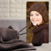 A smiling girl wearing a brown knitted hat and sweater, with a dark gray knitted blanket in the foreground.