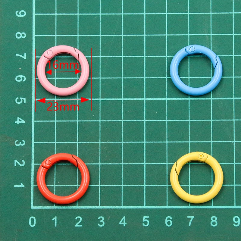 A collection of metal O-ring spring clasps in pink, blue, orange, and yellow are laid out on a green grid.