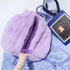 A fluffy purple pygmy hippo plush toy with a purple zipper and a light brown textured handle.