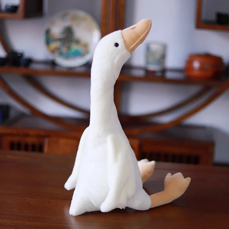 A white goose plush toy with a long neck is sitting on a wooden surface.