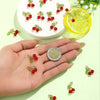 A hand holds various red cherry glass charms and a slice of lime on a light green background.
