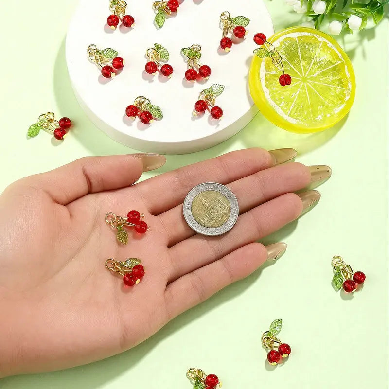 A hand holds various red cherry glass charms and a slice of lime on a light green background.
