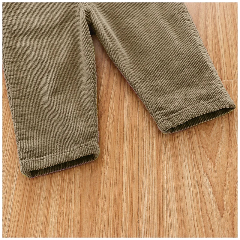A close-up of olive green baby cotton overalls with ribbed fabric texture lying on a wooden surface.