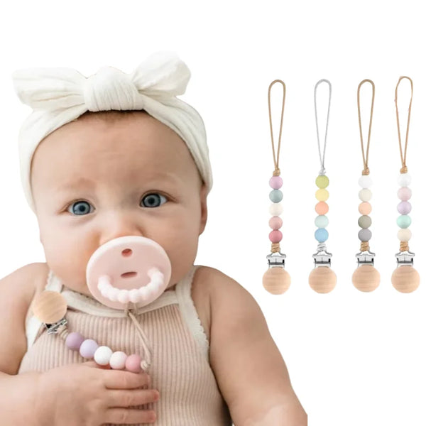 A baby is shown holding a silicone pacifier clip with multiple colored silicone pacifiers and clips.