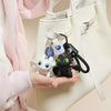 A hand holds a Toothless Dragon keychain featuring movable wings and glowing eyes against a white handbag.