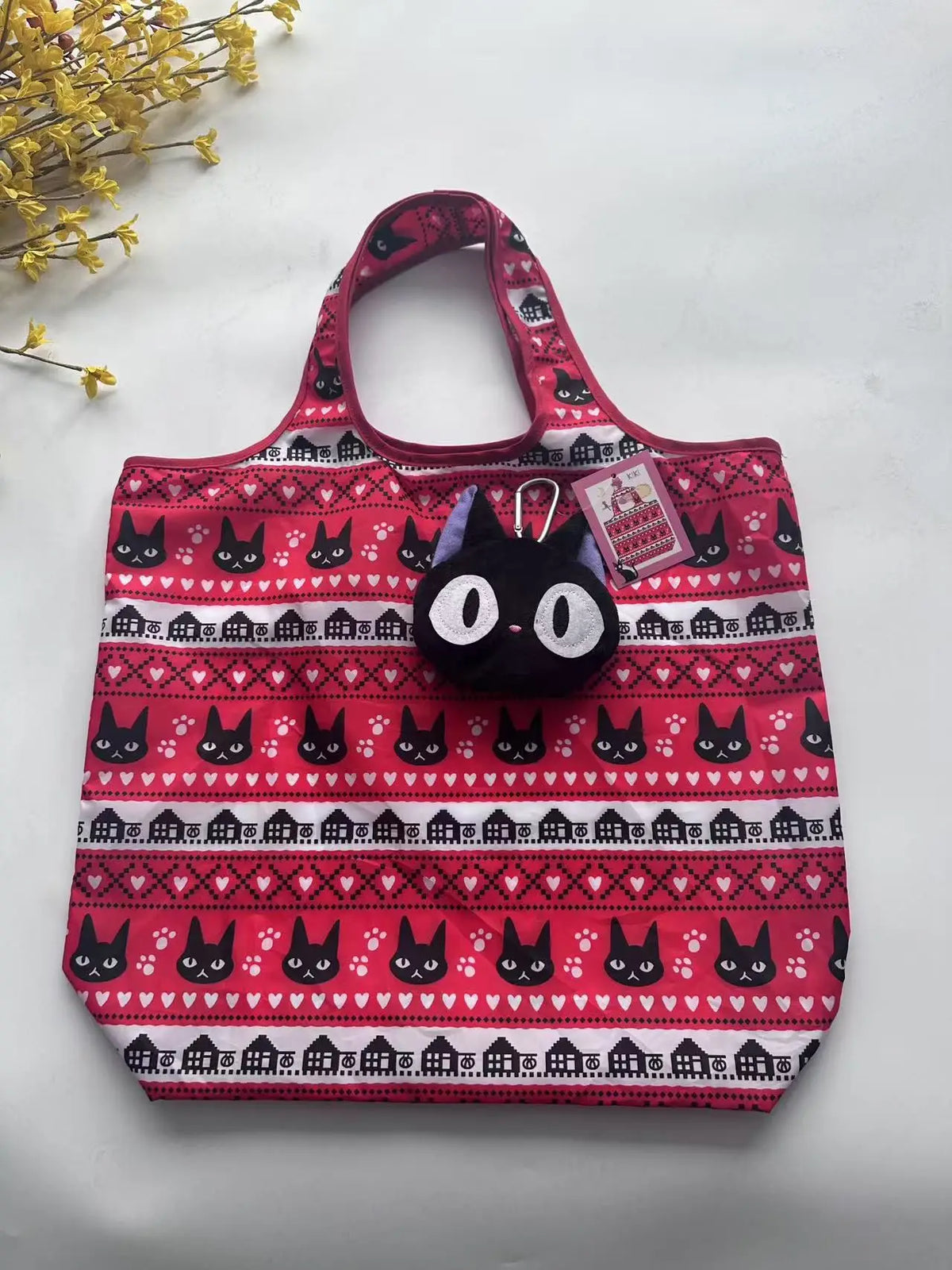 A pink and black patterned tote bag featuring a repeating cat design, placed on a white surface.