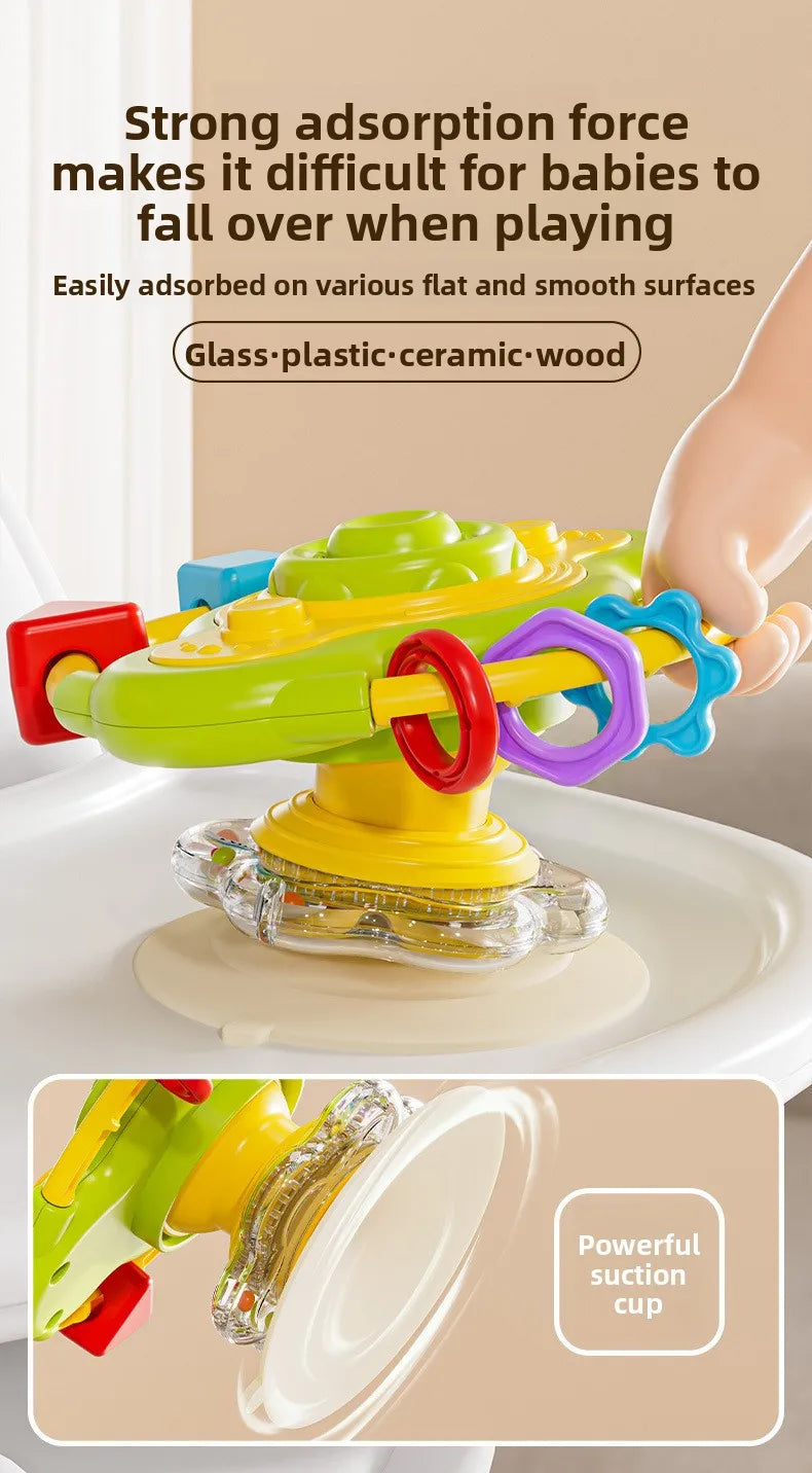 A bright green and yellow cartoon baby rattle toy with a suction cup is shown being played with by a hand.