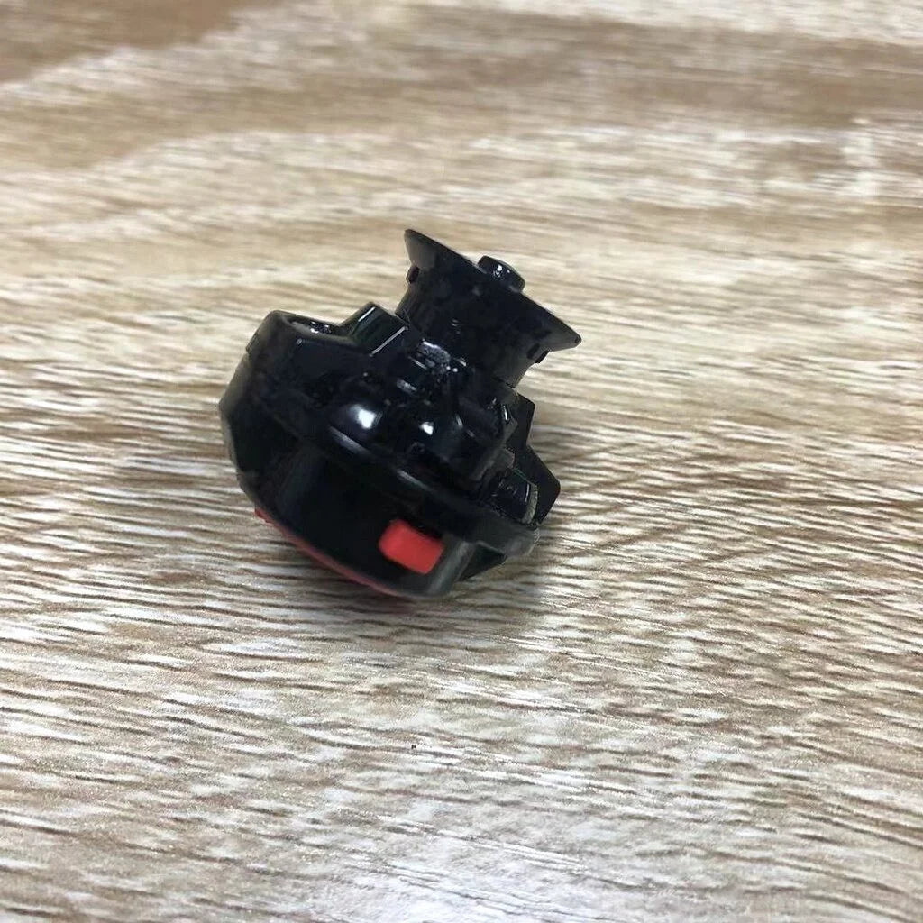 A black gyro driver for spinning tops with a red switch, placed on a light wooden surface.