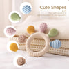 Silikon-Teether-Ring mit verschiedenen süßen Formen in Gelb, Pink, Grün und Blau auf weißem Stoff.