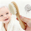 Una mano sostiene un peine de madera de haya natural cerca de la cabeza de un bebé sonriente para el cuidado del cabello reci