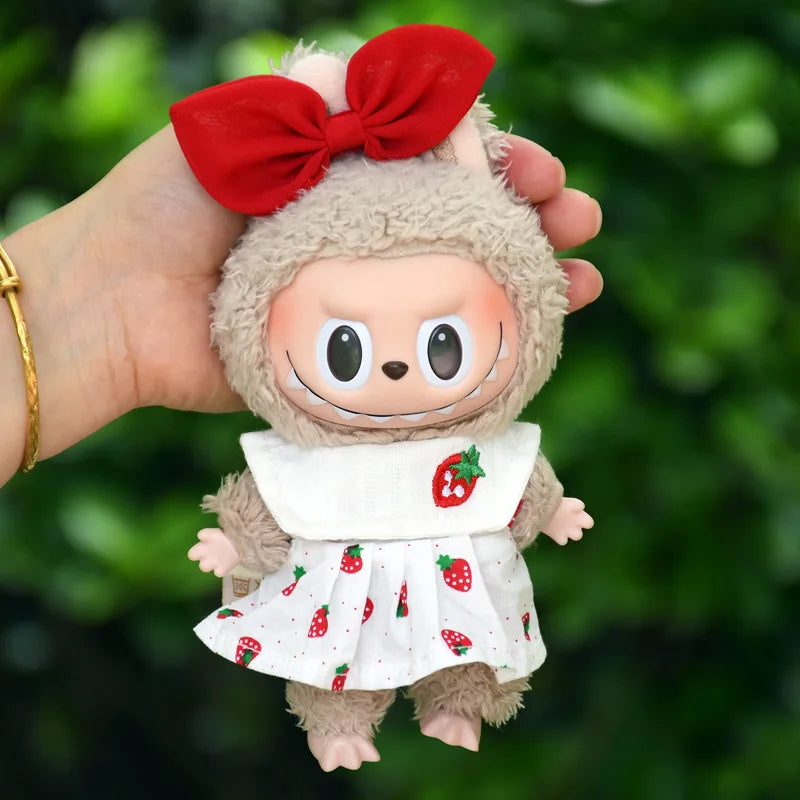 A plush doll dressed in a strawberry party outfit with a red bow and white dress, held in a hand.
