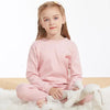 A young girl wearing a pink cotton pajama set with an astronaut print, sitting on white fur.