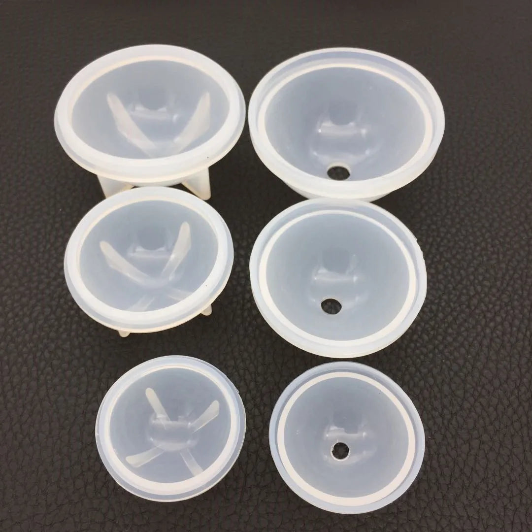 Four clear silicone molds shaped like spheres or cups for resin crafting