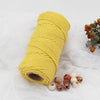 A yellow natural cotton macrame rope coiled tightly on a white fabric surface.