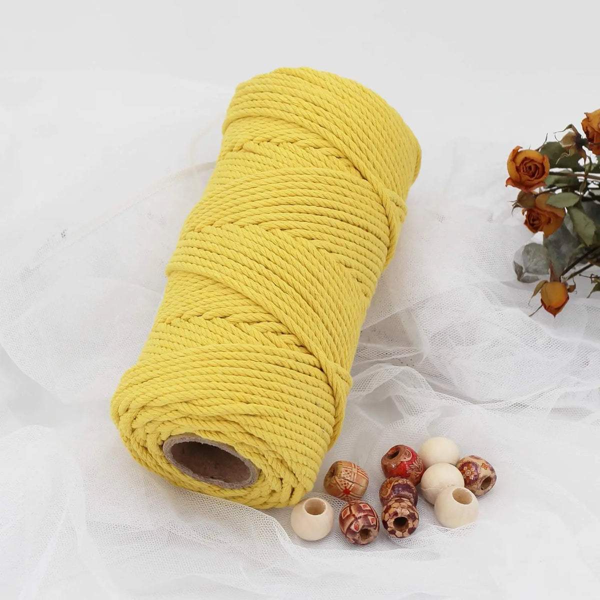A yellow natural cotton macrame rope coiled tightly on a white fabric surface.