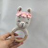 A handmade knitted deer rattle and teether ring with pink flowers, held in a hand.